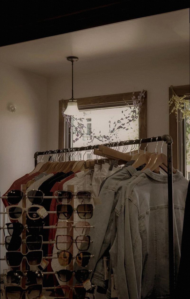 Stylish fashion store with sunglasses and clothes on racks under warm lighting.